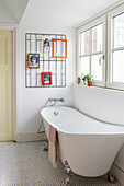 Freestanding bathtub in light-coloured bathroom with wall decor and window view