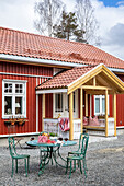 Rotes Holzhaus mit überdachtem Eingang und grüner Sitzgruppe im Vorgarten