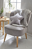 Grey armchair with star cushion and faux fur, side table with candles and cup