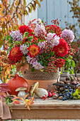 Autumn table decoration with flowerpot of dahlias, roses, rose hips, mushrooms and pumpkin
