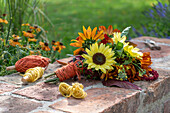 Blumenstrauß mit Sonnenblumen (Helianthus), Brokkoli, Fuchsschwanz (Amaranthus) auf Gartenmauer und Garn