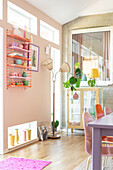 Colourful dining area with retro shelf and floor lamp in front of pink wall