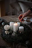 Hand lights a white candle in an Advent arrangement