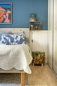 Bed with patterned pillows in a bedroom with blue walls and artwork