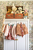 Children's room with vintage wardrobe, old suitcase, cuddly toys and clothes on hangers