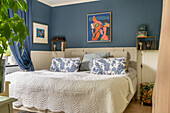 Double bed with patterned cushions in bedroom with dark blue wall