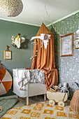 Children's room with wall paint and wallpaper in green and canopy over white crib