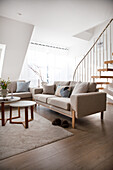 Helles Wohnzimmer mit modernem Sofa, beigem Teppich und Holztreppe