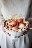 Bowl of fresh eggs held in hands on straw