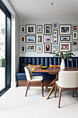 Fotogalerie über Sitzbank aus blauem Kunstleder, Esstisch aus Nussbaum und weiße Stühle im Essbereich