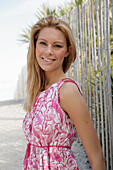 Blonde Frau in rosa-weißem Sommerkleid am Strand