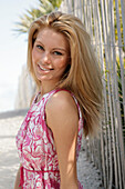 Blonde woman in pink and white summer dress on the beach