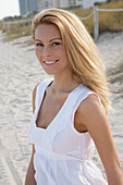 Blonde Frau in weißem Sommerkleid am Strand