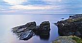 Rock And Tranquil Water Along The Coastline At Dawn; Orkney, Scotland