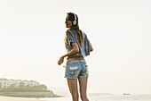 Junge Frau, die mit ihren Kopfhörern am Strand Musik hört; Xiamen, China