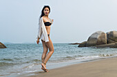 Junge Frau, die im Bikini am Strand spazieren geht; Xiamen, China