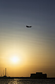 Airplane Flying Over The Harbour At Sunset; Paphos, Cyprus