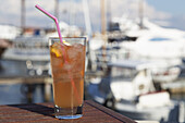A Glass Of Iced Tea On A Table With Boats In The Harbour In The Background; Paphos, Cyprus