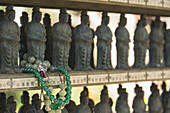 Ein buddhistisches Armband, das um eine Tempelfigur unter vielen anderen gewickelt ist; Ohara, Kyoto, Japan