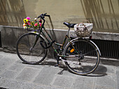 Ein vor einem Gebäude geparktes Stadtrad, geschmückt mit Blumen und einem Korb; Florenz, Italien