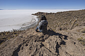 Frau sitzt auf einer Insel aus Felsen und Kakteen namens Incahuasi; Uyuni, Bolivien