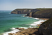 Felsige Küstenlinie und Bucht mit Turm im Hintergrund und blauem Himmel; Frehel, Bretagne, Frankreich