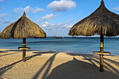 Strandpalapas am Palmenstrand mit Segelbooten, die nahe am Ufer verankert sind; Aruba