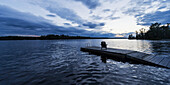 Silhouette eines Adirondack Chair auf einem hölzernen Dock entlang eines Sees bei Sonnenuntergang; Ontario, Kanada