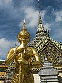 Verziertes Gebäude mit Turmspitze und einer goldenen Statue im Vordergrund, Tempel des Smaragdbuddhas (Wat Phra Kaew); Bangkok, Thailand