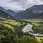 Ein Fluss, der durch ein Tal mit üppigem Ackerland fließt, das von Bergen umgeben ist; Punakha, Bhutan