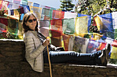 A Woman Rests On A Wall Beside Colourful Prayer Flags; Paro, Bhutan
