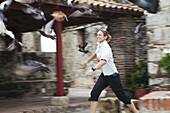 Eine junge Frau läuft einem Vogelschwarm hinterher, der gerade fliegt; Cartagena, Kolumbien