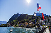 Sonnenschein auf der italienischen Flagge und Blick aufs Wasser von der Stadt Menaggio am Comer See; Menaggio, Lombardei, Italien