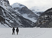 People Walking On Frozen Lake Louise With A View Of The Snow Covered Mountains; Lake Louise, Alberta, Canada