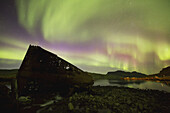 Nordlichter über der Stadt Djupavik entlang der Strandir-Küste, hier tanzen sie über der alten Heringsfabrik und dem Schiffswrack; Djupavik, Island