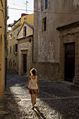 Mädchen, das eine Kopfsteinpflastergasse zwischen Gebäuden entlanggeht; Alghero, Sardinien, Italien