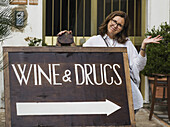 Eine Frau posiert mit einem Schild für Wein und Drogen; Ravello, Italien