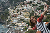 Eine Frau posiert mit Blick auf die Gebäude entlang der Amalfiküste; Positano, Kampanien, Italien