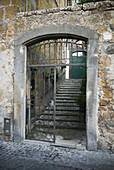 Abgenutzte und verwitterte alte Steinmauern mit einem offenen Tor, das zu einer Treppe und einer grünen Tür führt; Orvieto, Umbrien, Italien