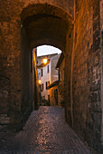 Ein schmaler überdachter Weg aus Kopfsteinpflaster, der in der Abenddämmerung zu einem Licht und Häusern führt; Orvieto, Umbrien, Italien