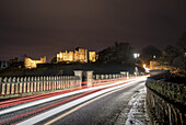 Lichtspuren auf einer Straße und beleuchtete Gebäude im Hintergrund zur Nachtzeit; Alnwick, Northumberland, England