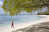 Frau im Bikini spazierend am Ufer eines weißen Sandstrandes