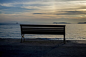 Silhouette Of A Bench At The Water's Edge On A Beach At Sunset Along The Aegean Sea; Panormos, Thessalia Sterea Ellada, Greece