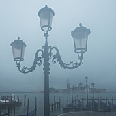 Verschnörkelter Laternenpfahl und Markusplatz im Nebel; Venedig, Italien