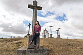 Eine chinesische junge Frau, die auf einem Kreuz in der Umgebung von Segovia sitzt; Segovia, Kastilien-León, Spanien