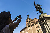 An Asian Young Woman Taking A Picture Of San Martin Church And Juan Bravo Statue, Romanic Style Construction; Segovia, Castilla Leon, Spain