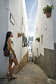 Eine junge chinesische Frau steht vor einem weißen Wohnhaus in einer engen Straße; Mojacar, Almeria, Spanien