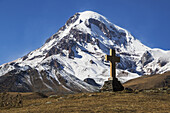 Stone Cross With Mount Kazbek In The Background; Kazbegi, Mtskheta-Mtianeti, Georgia