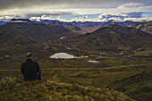 Mann auf einem Aussichtspunkt mit Blick auf das Blackstone Valley, entlang des Dempster Highway; Yukon, Kanada