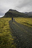 Mann, der einen Schotterweg entlang der Südküste Islands entlanggeht; Island